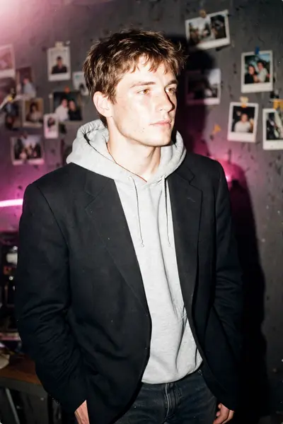 ULTRA-REALISTIC 1990s-STYLE CANDID FLASH PORTRAIT of the same young man, same face, hairstyle and skin tone, wearing an oversized hoodie under a